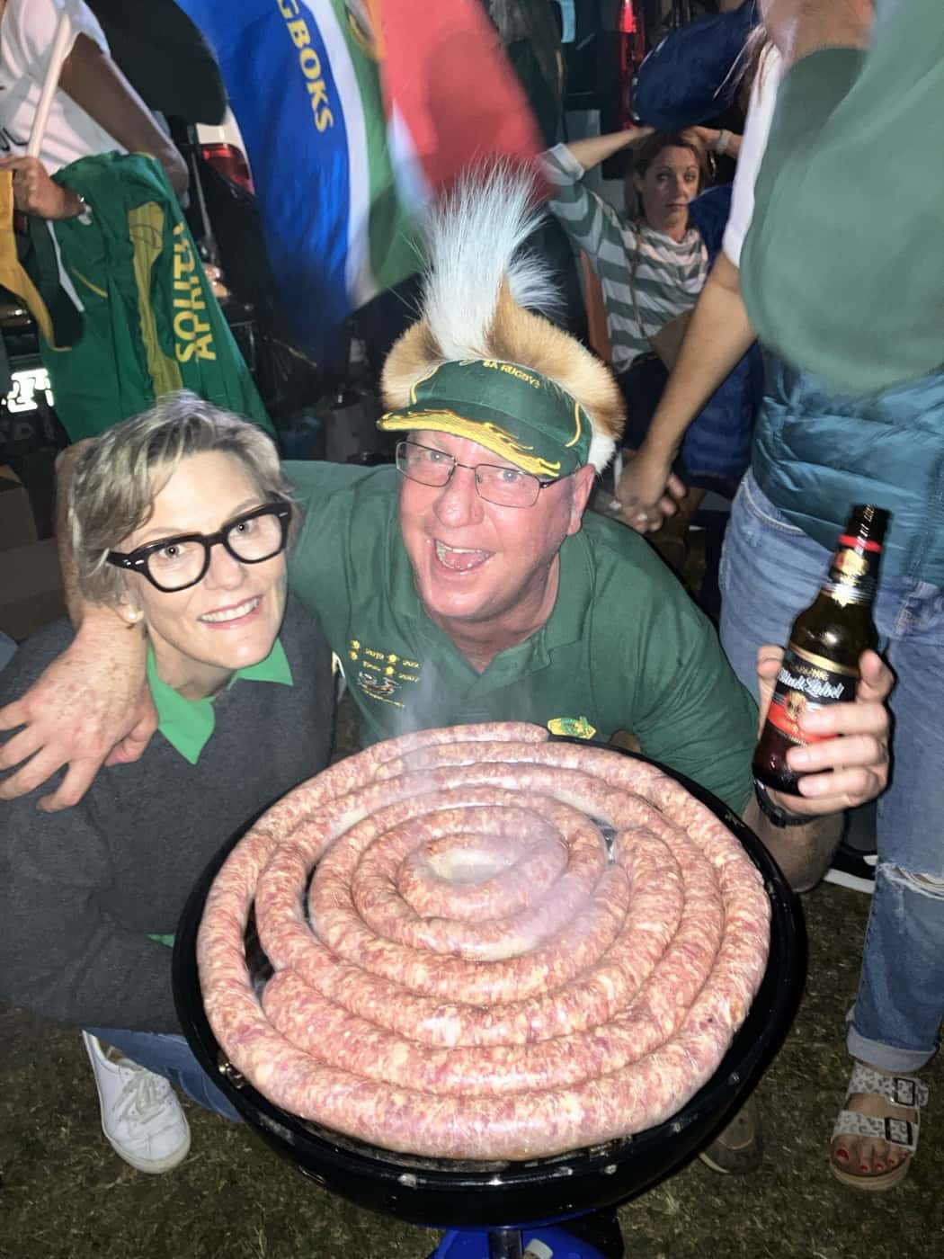 A braai in the dark on a Springbok match night, boerewors coiled on the grill