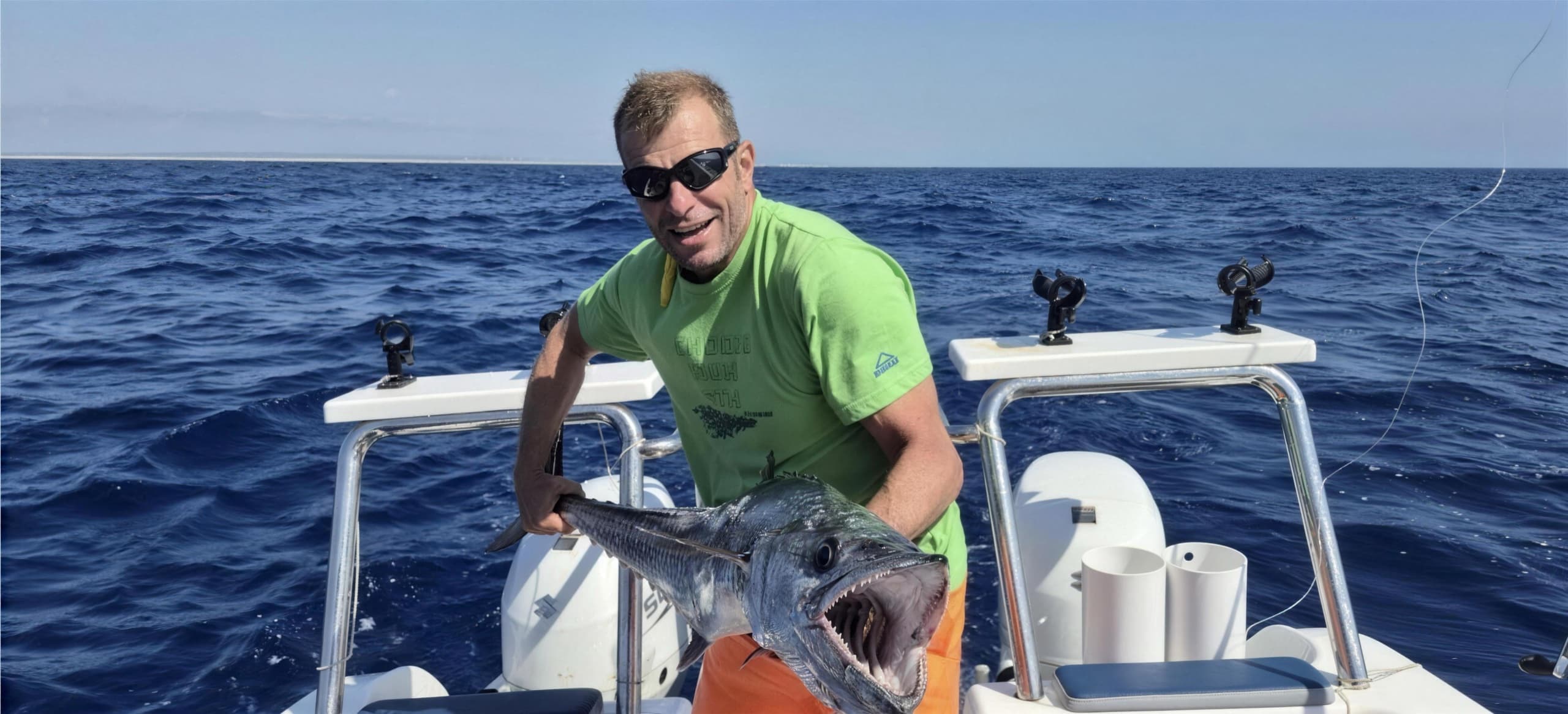 An angler at the stern of a boat holding a large game fish, open blue water off Vilanculos with the Mozambique coastline low on the horizon