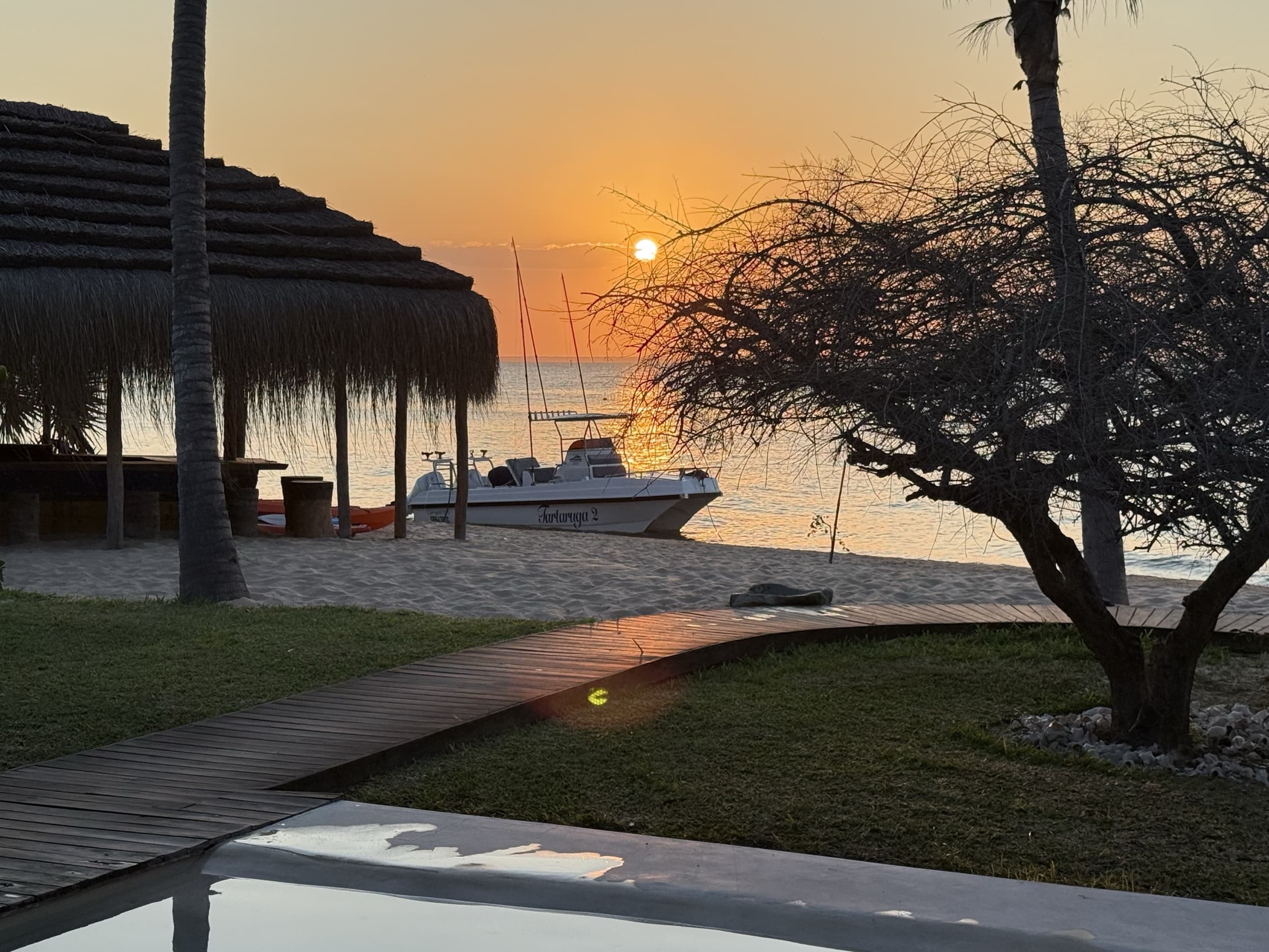 The lodge at sunset: thatched roofs, a fishing boat pulled up on the beach and the sun going down over the bay