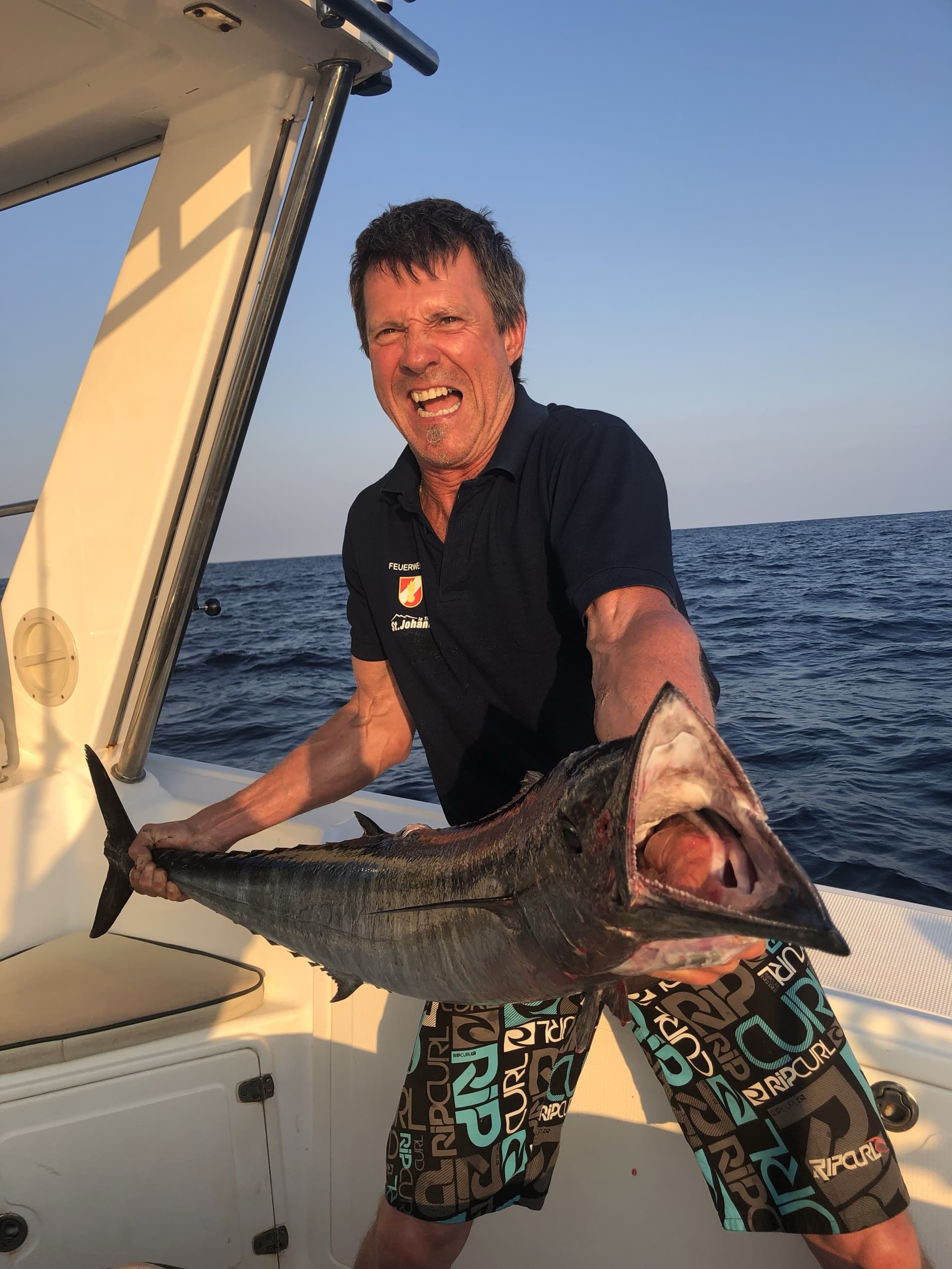 A guest holding a wahoo on the deck of the boat in the evening light, open water behind him