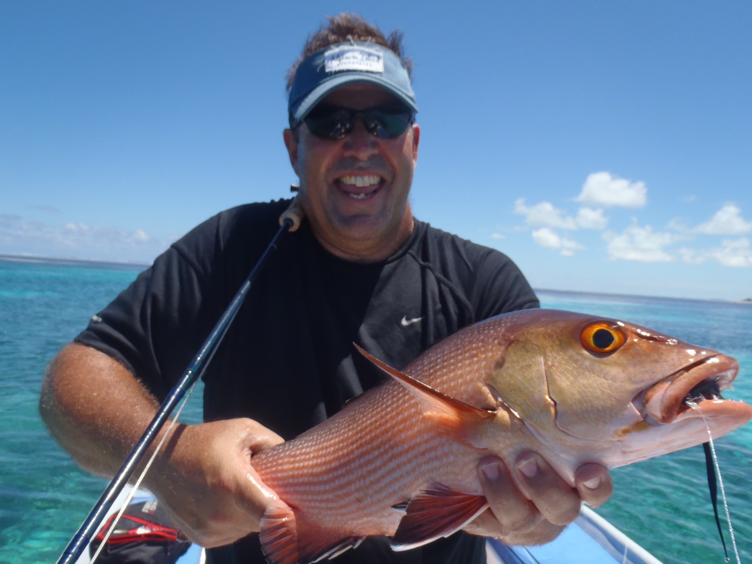 A guest on the boat holding a red reef fish, turquoise water and a low sandbank behind him