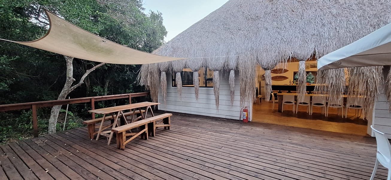 The wooden deck at Casa Bella with benches under a shade sail and the thatched, open-fronted bar and dining room behind