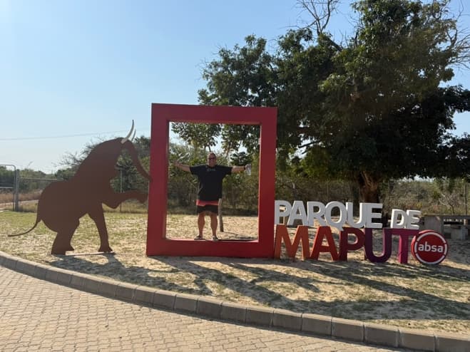Gordy standing inside the red picture frame at the Parque de Maputo entrance sign, next to a steel elephant silhouette